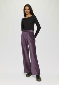 Brede broek van zacht, pluizig paars materiaal, met zijzakken en een hoge taille; gecombineerd met een aansluitend zwart longsleeve shirt.