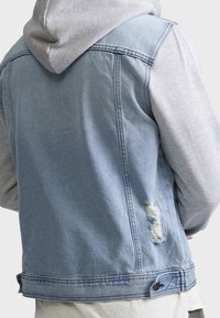 Chaqueta vaquera con capucha gris, de color azul claro, detalles desgastados en la parte trasera, cierre con botones en el dobladillo y texturas contrastantes entre materiales.