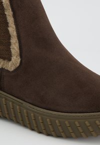 Braune Wildleder-Stiefelette mit einem flauschigen beigen Seitenpaneel, strukturiertem Gummisohle und verstärkter Naht für Langlebigkeit.