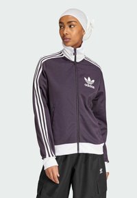 Chaqueta de chándal Adidas en color morado oscuro con detalles en blanco, con cremallera frontal, cuello alto y tres rayas blancas en cada manga.