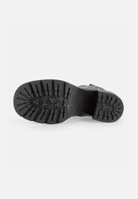 Suela de bota de goma negra con bandas profundas, con patrones ovalados y triangulares para mayor agarre; talón reforzado y bordes lisos.
