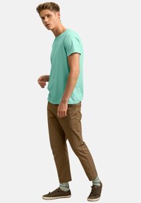 T-shirt turquoise à manches courtes associé à un pantalon marron clair et des baskets foncées, avec des chaussettes à motifs. Couverture simple et coupe confortable.