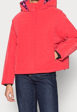 Chaqueta acolchada roja con capucha forrada que presenta un interior de patrón rosa, mangas largas y bolsillos frontales, combinada con jeans de color azul oscuro.
