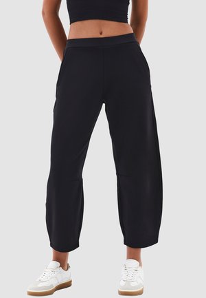 Black relaxed-fit cropped pants with a flat waistband, side pockets, and a smooth texture, paired with white sneakers.