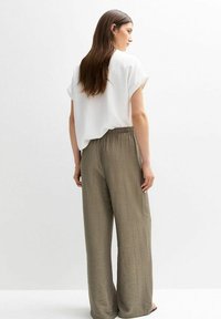 Haut blanc à manches courtes ; coupe décontractée. Pantalons olive à jambe large avec une finition texturée et une taille élastique. Vue arrière du mannequin.