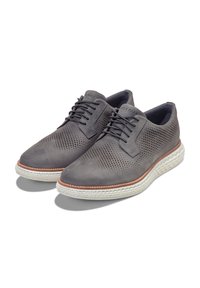 Zapatos de cuero gris perforado con punta redonda, cordones de cuero y una suela texturizada de color claro. Presentan costuras decorativas alrededor de la suela.