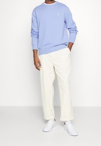 Ljusblå sweatshirt, vita byxor med elastisk midja och vita slip-on skor. Enkel design, mjuk textur och inga synliga mönster.