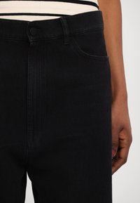 Jeans de mezclilla negra con una cintura de altura media, bolsillos frontales y detalles de costura sutiles. La tela tiene una textura suave y un ligero estiramiento.