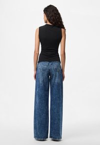 Μαύρο αμάνικο τοπ με εφαρμοστή σιλουέτα, σε συνδυασμό με μπλε τζην παντελόνι με φαρδιά μπατζάκια, ελαφρύ ξέβγαλμα και εμφανείς πίσω τσέπες.