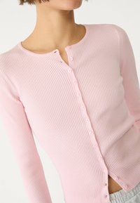 Różowy prążkowany kardigan z długim rękawem, z okrągłym dekoltem, zapinany na guziki z przodu, z delikatnymi rozcięciami po bokach u dołu.