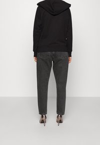 Svart hoodie med huva, kombinerad med högmidjade, mörkgrå jeans i denim och spetsiga klackskor; minimalistisk design, slät textur.