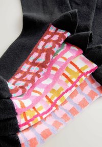 Satz von fünf Paar Socken in verschiedenen Farben und Mustern, darunter Schwarz, Pink und Braun. Weiche Textur mit markanten, grafischen Designs.