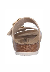 Sandale en daim beige avec deux boucles ajustables en métal doré et une semelle en liège. Semelle extérieure en caoutchouc blanc et intérieur doux et texturé.