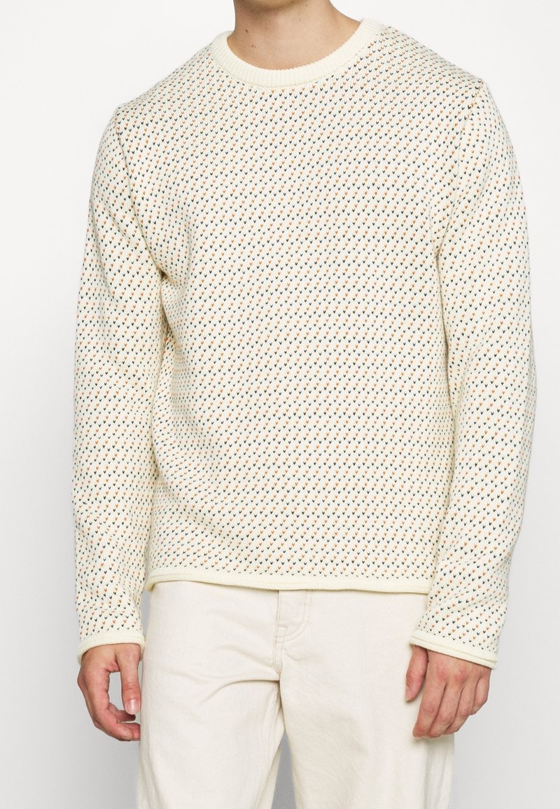 En krämfärgad stickad tröja med ett texturerat mönster av små färgade trianglar i orange och blått. Ribbad halsringning och manschetter. Regular fit.