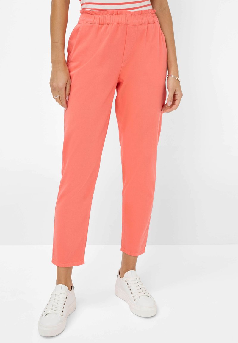 Koraalvormige tapering broeken met een elastische tailleband, zijzakken en een gladde textuur, gecombineerd met witte sneakers.