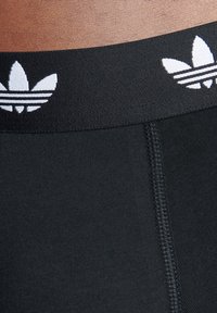 Svart atletisk underkläder med en texturerad midja med en vit logotyp och tre ränder mönster. Sömmarna syns på tyget.