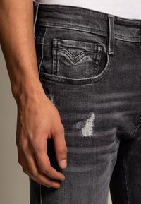 Černé džíny z denimu s detailem poškozeného kolena, mají zadní kapsu s kontrastním prošitím a úzký střih.