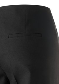 Nahaufnahme von schwarzen, maßgeschneiderten Hosenrückseiten mit einer aufgesetzten Tasche und Nahtdetails auf glattem Stoff.
