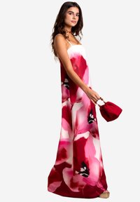 Blumenkleid im Maxistil mit rosa und roten Farbtönen, mit Spaghetti-Trägern und fließender Silhouette. Accessoires mit einer gerafften roten Handtasche.