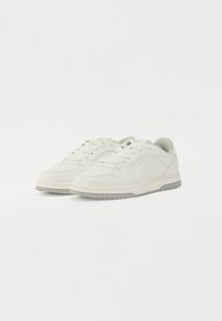 White leather sneakers with a smooth texture, rounded toe, and padded tongue. Light gray sole with a patterned tread and minimal branding.