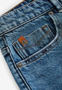 Jeans din denim, cu o nuanță albastră decolorată, o mică buzunar frontal, accente din piele maro și accesorii din metal argintiu, cu cusături vizibile.