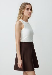 Weiße ärmellose Bluse mit Rundhalsausschnitt, kombiniert mit einem dunkelbraunen ausgestellten Rock. Beide Kleidungsstücke zeichnen sich durch glattes Material und figurbetonte Silhouetten aus.