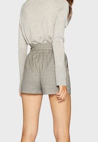 Pantaloni corti grigi a quadretti con una cintura elasticizzata, abbinati a una maglietta a maniche lunghe grigio chiaro; texture semplice, vestibilità comoda, lunghezza sopra il ginocchio.