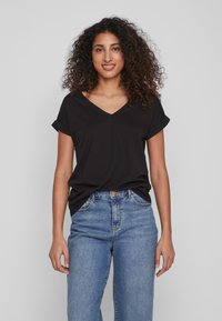 Juoda V-kaklo t-shirt su sukamu trumpomis rankovėmis, pagaminta iš švelnios medžiagos. Derinama su aukštu liemeniu mėlynomis džinsinėmis kelnėmis, turinčiomis klasikinį penkių kišenių dizainą.