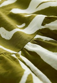 Rochie din bumbac cu o bază de culoare verde măslin, având dungi albe ondulate îndrăznețe. Include plii pentru textură și mișcare. Suprafață netedă.