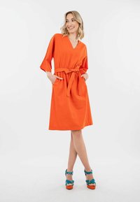 Oranje jurk met korte mouwen, een V-hals, een getailleerde taille en zijzakken. Heeft een ceintuurd ontwerp en een loose fit, gemaakt van lichte stof.