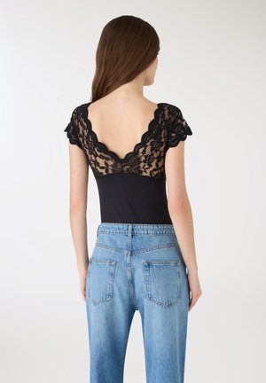 Czarny bodysuit z koronkowym tyłem, z głębokim dekoltem w kształcie litery V, krótkimi falbankowymi rękawami, zestawiony z jasnoniebieskimi, wysokim stanem jeansami.