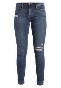 Dark blue skinny jeans with distressed patches on upper left thigh and right knee, five-pocket design, button and zipper closure.