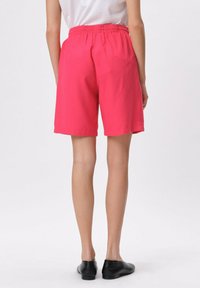 Różowe spodenki z elastycznym pasem, do kolan, o gładkiej teksturze. W parze z czarnymi płaskimi butami. Prosty, nieozdobiony design.