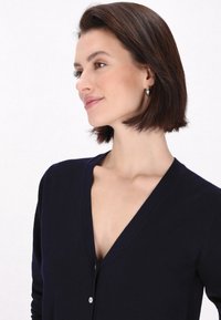 Cardigan blu navy con scollo a V, caratterizzato da un tessuto lavorato a maglia e una singola colonna di bottoni. Tessuto liscio e design aderente con maniche lunghe.
