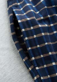 Tissu à carreaux bleu, marron et blanc avec une ouverture de poche latérale visible sur un fond gris clair.
