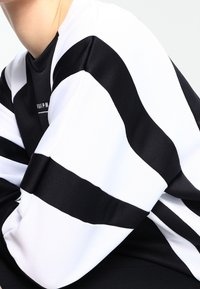 Svart- och vitrandig sweatshirt med djärva horisontella ränder, strukturerad textil, rund halsringning och en diskret logotyp på framsidan.