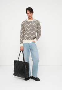 Svetar s uzorkom u smeškastim i krem tonovima u cik-cak obliku, svijetloplave traperice i velika crna kožna torba s dvije drške. Jednostavna pozadina.