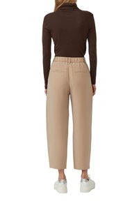Beige weite Hosen mit elastischem Bund, zwei Gesäßtaschen, kombiniert mit einem dunkelbraunen Rollkragenpullover und weißen Plateau-Sneakern.