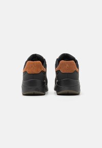 Încălțăminte sport neagră cu accent de călcâi din suede maro și talpă din cauciuc texturat. Designul include un guler căptușit pentru confort.