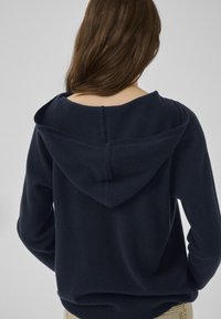 Navyblauer Kapuzenpullover aus weichem Stoff, mit lockerem Schnitt und sichtbarer Naht entlang des Rückens. Glatte Textur und schlichtes Design.