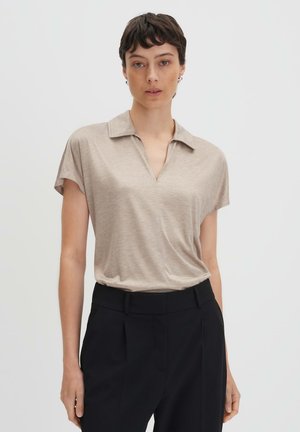 Polo beige à manches courtes avec un col en V et une texture douce, associé à un pantalon noir ajusté. Design épuré et minimaliste.