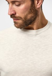 Helles beiges Sweatshirt mit strukturiertem Strickmuster, Rundhalsausschnitt und gerippten Bündchen. Der Stoff wirkt weich und leicht elastisch.