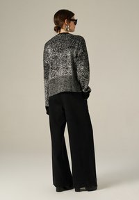 Maglione lavorato a maglia bianco e nero con pattern testurizzato, vestibilità over e orlo a coste. Abbinato a pantaloni neri a gamba larga a vita alta.
