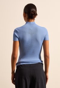 Hellblauer, gerippter Pullover mit hohem Kragen, kurzen Ärmeln und figurbetontem Design, der vertikale Textur- und Nahtdetails auf der Rückseite zeigt.