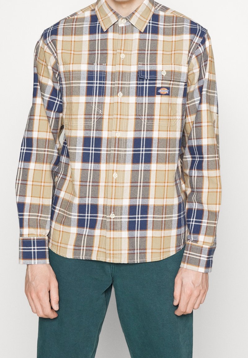 Camicia a maniche lunghe a quadri in beige, blu navy e grigio con dettagli arancioni. Presenta un colletto con bottoni e due tasche sul petto.