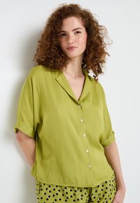 Camicia a maniche corte con bottoni di un verde vivace, realizzata in tessuto morbido, con una vestibilità rilassata, colletto a toppa e maniche arrotolate.