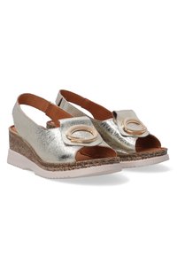 Slingback wedge sandalen in metallic goud met open neus, cirkelvormige accentdetails, gestructureerde kurken middenzool en witte rubberen buitenzool.