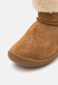 Bottes en suède marron avec un bout arrondi, dotées d'un col en fourrure crème douce et d'une semelle en caoutchouc flexible.