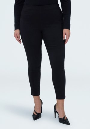 Czarne dopasowane spodnie o gładkiej fakturze i wysokim stanie, zestawione z czarnymi czółenkami na wysokim obcasie z odkrytymi palcami.