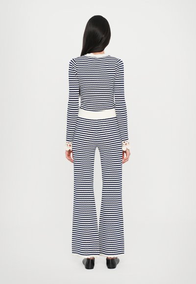 Set format din bluză cu mâneci lungi și pantaloni evazați, în nuanțe de bleumarin și alb. Are talie ajustată și dantelă pe manșete. Material neted și elastic.